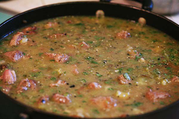 Pork, oregano, tomatillo sauce, stock, and ground cloves cooking in a skillet