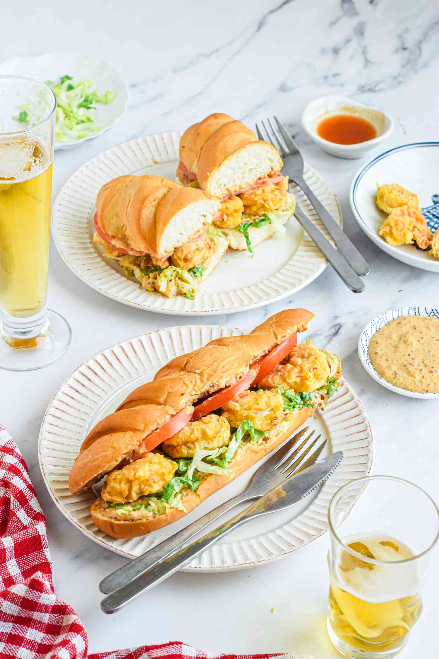 Classic Shrimp Po Boy Sandwich on a Plate, Surrounded by Glasses of Beer, Another Plate with a Halved Shrimp Po Boy Sandwich, and a Small Saucer of Remoulade