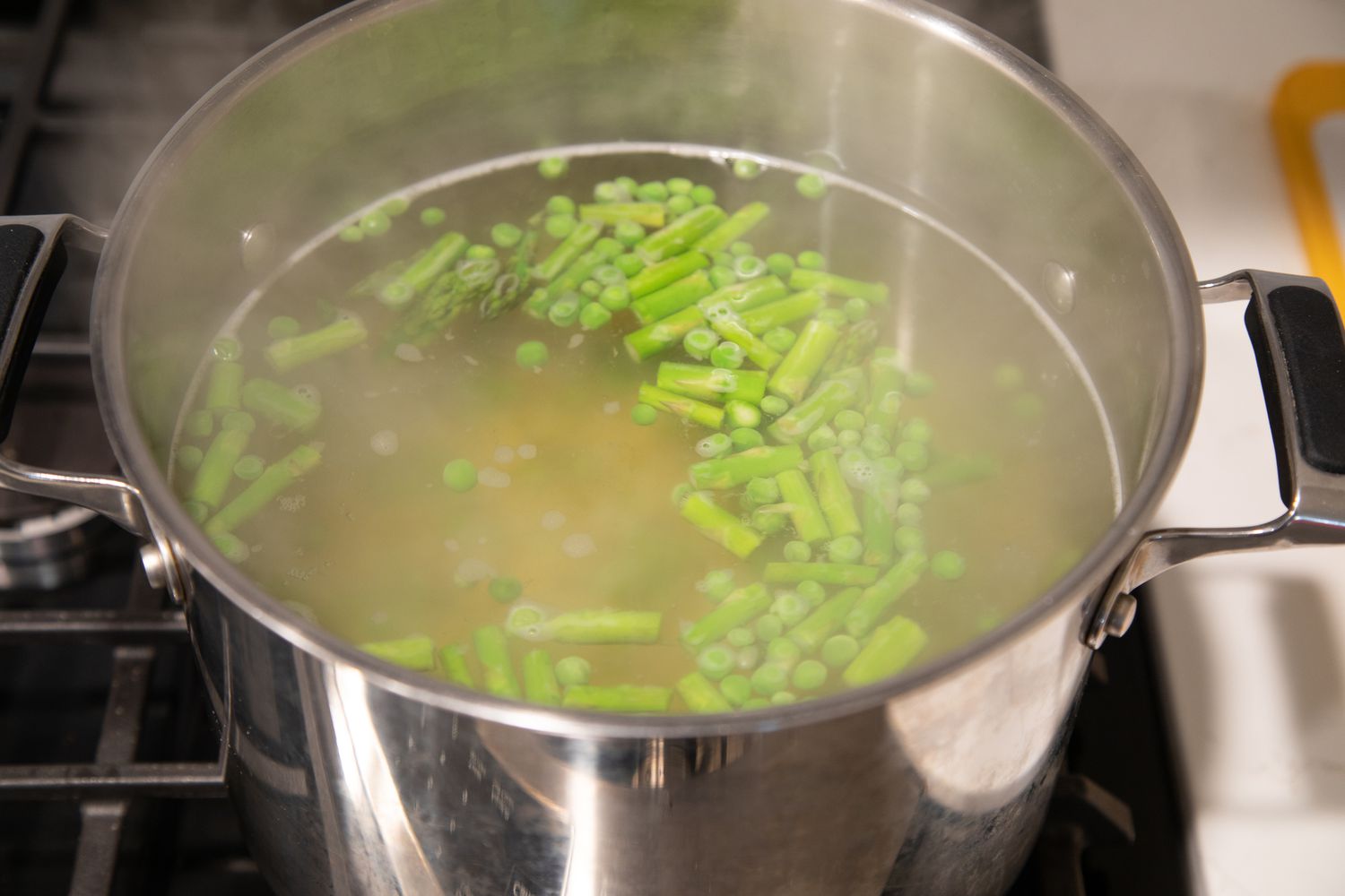 A pot of boiling water with asparagus pieces being cooked on a stovetop