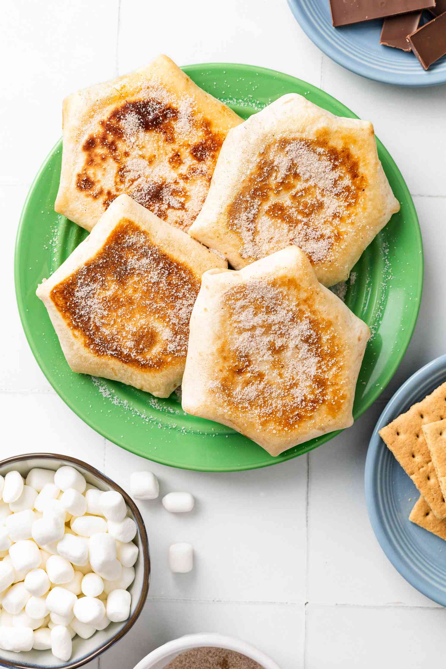 S'more Crunchwrap on a Plate, and in the Surroundings, Bowl of Mini Marshmallows, Bowl of Chocolate Bars, and a Plate With Graham Crackers