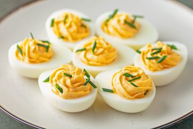 Deviled eggs topped with chopped chives served on a white plate