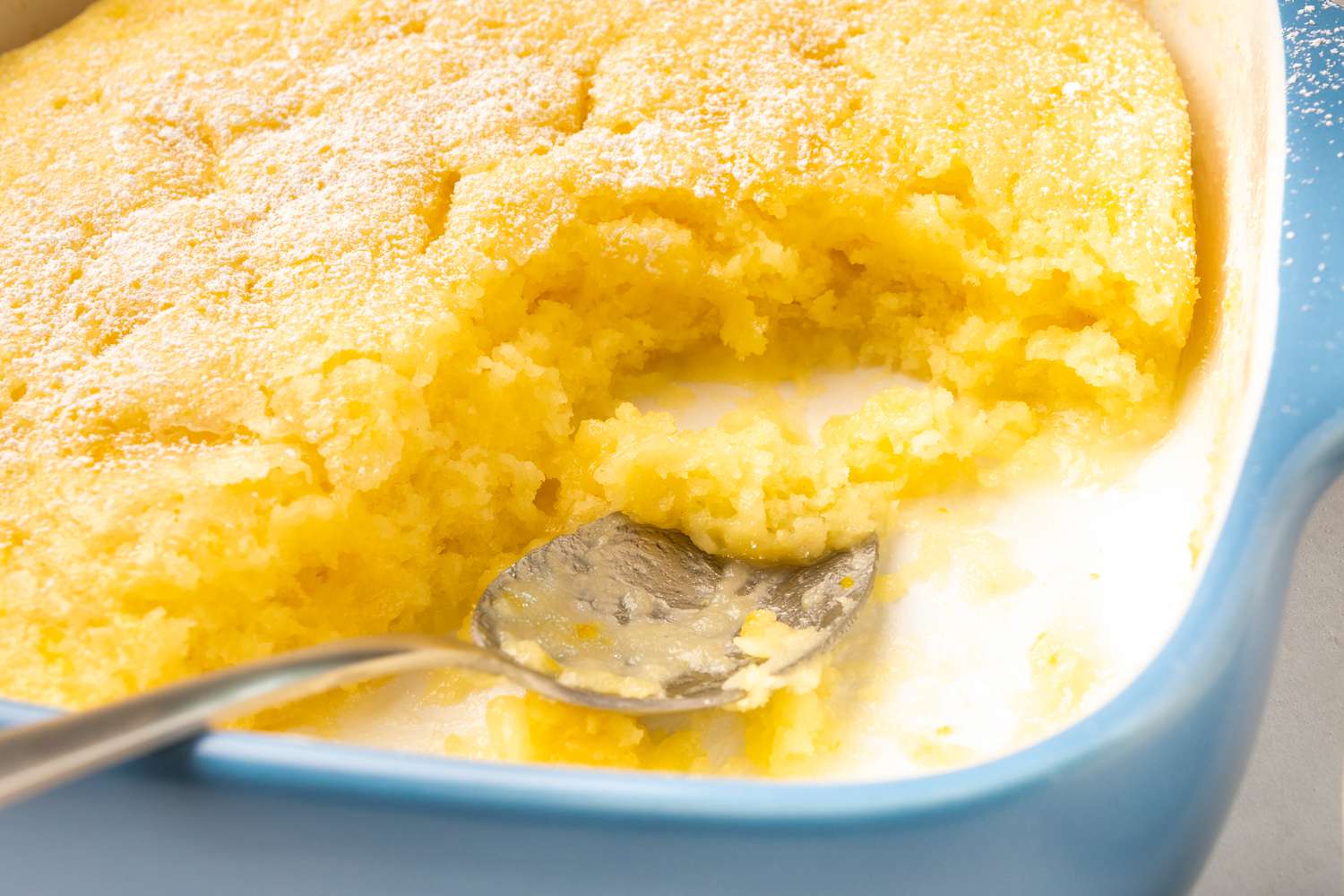 Closeup of a baking dish with lemon pudding cake, corner of the cake scooped out