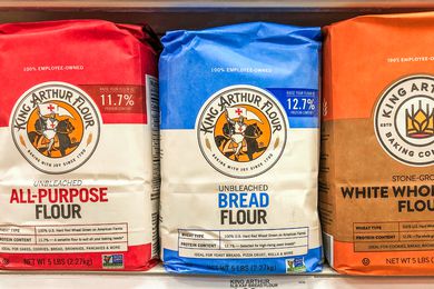 Bags of King Arthur brand flour on a store shelf, displaying different types such as all-purpose, bread, and whole wheat
