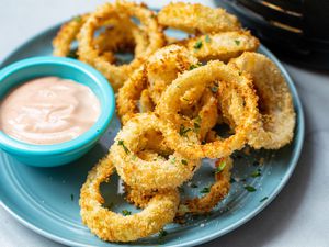 Crispy Air Fryer Onion Rings stacked on a plate with a dipping sauce.