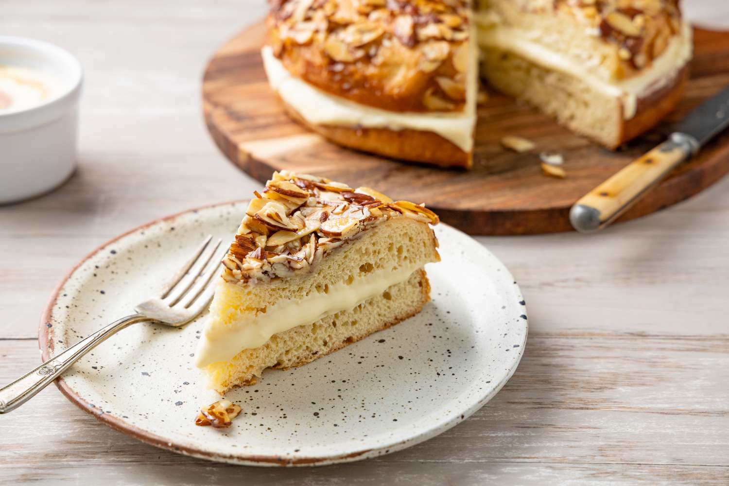 Slice of Bee Sting Cake on a Plate with a Fork with the Rest in the Background on a Circular Board