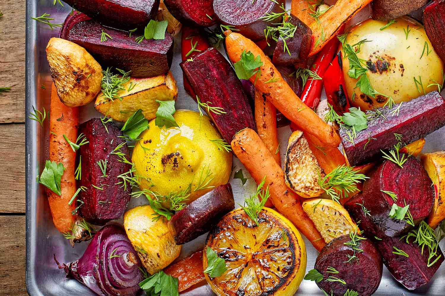 A mix of vegetables roasted on a sheet pan—beet wedges, carrots, potato wedges, and lemon halves, all garnished with parsley and dill