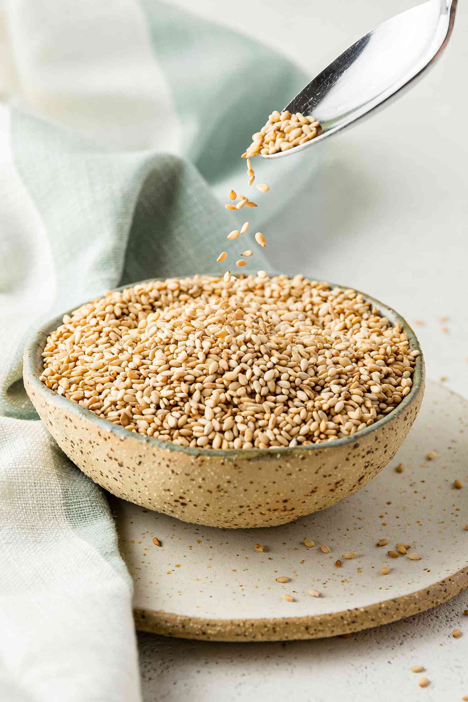 Toasted Sesame Seeds in a Bowl with Some Cascading into the Bowl from a Spoon