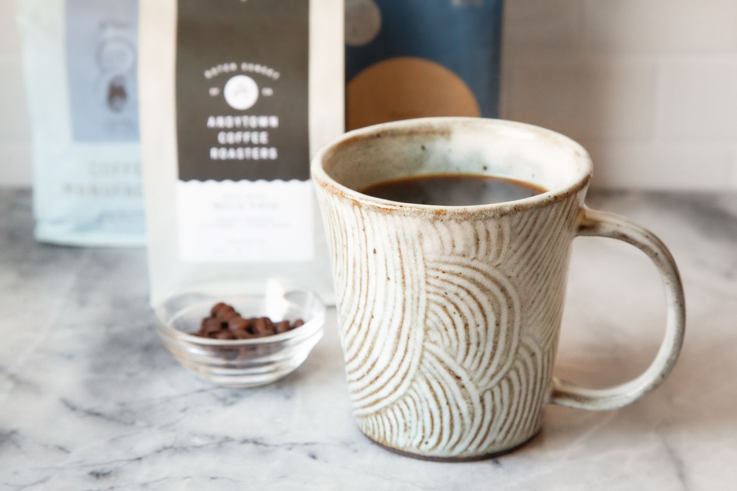 Cup of Decaffeinated Coffee, Three Bags of Coffee Beans, and a Small Bowl with Coffee Beans