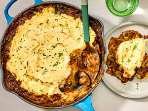 Overhead shot of lentil shepherd's pie in a skillet, with a serving spoon having scooped a serving of the dish out on a plate to the right of the skillet