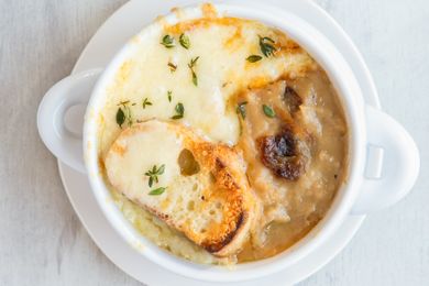 A bowl of French onion potato soup topped with melted cheese herbs and a slice of bread