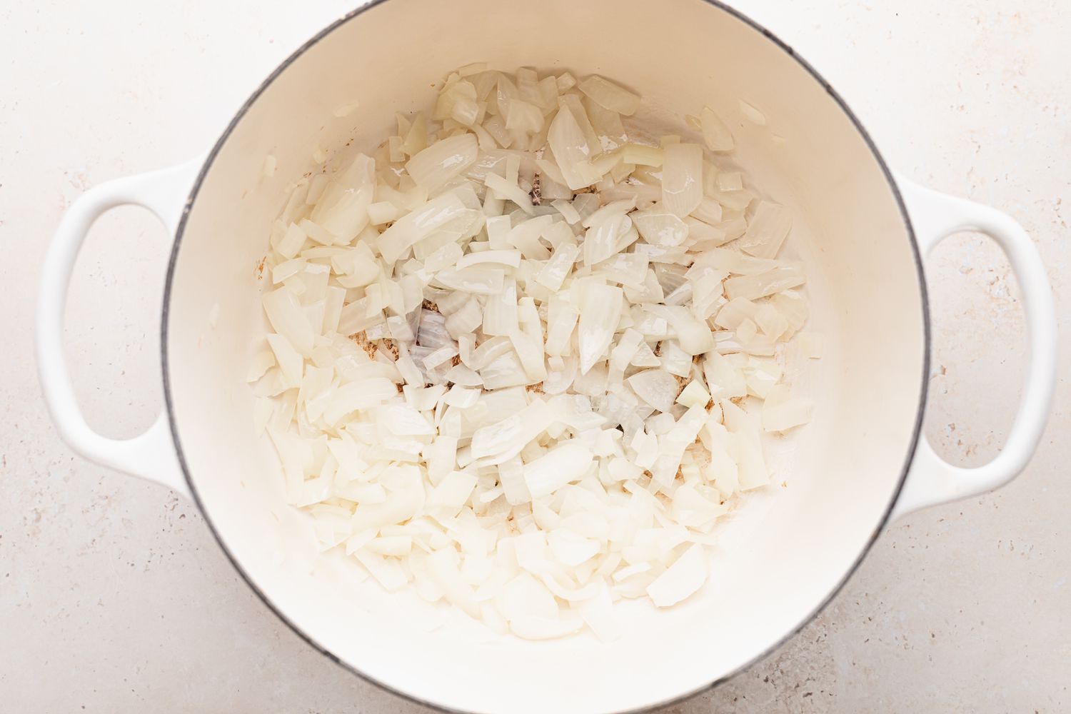 White dutch oven with onions to make white chicken chili recipe.
