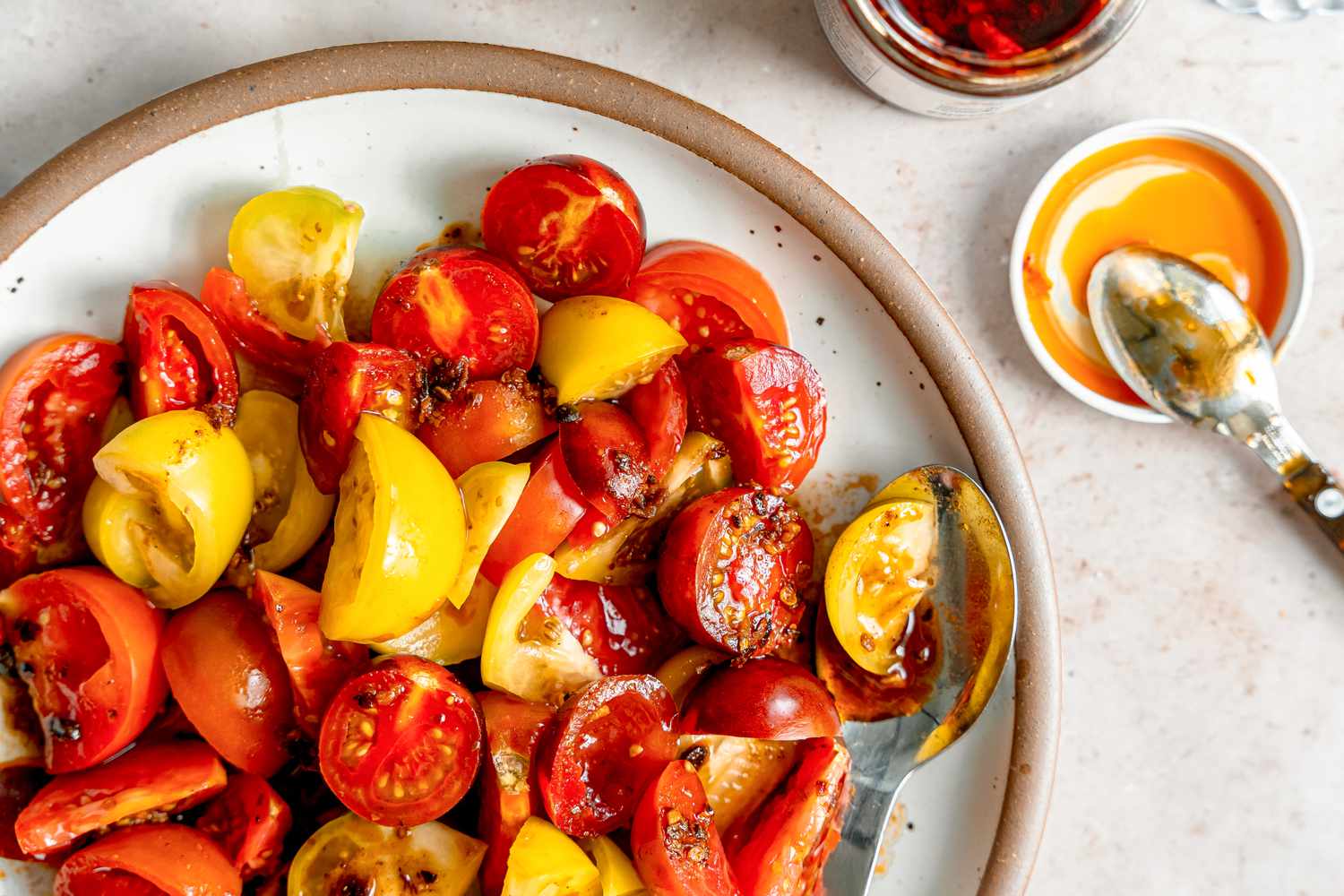 5-ingredient chili crisp tomato salad on a plate next to a jar of chili crisp and a spoon resting on the jar lid