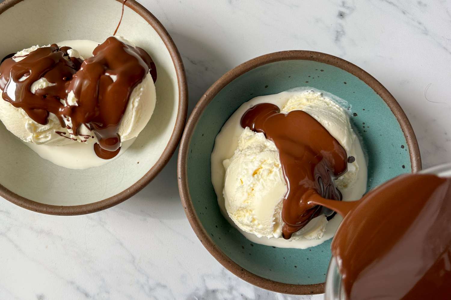Two bowls of ice cream with chocolate sauce being poured onto one