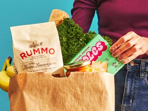 Paper bag of groceries, a woman's hand is pulling out a box of mac and cheese