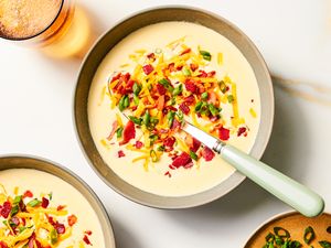 A bowl of loaded potato soup garnished with shredded cheese bacon bits and green onions with a spoon placed inside