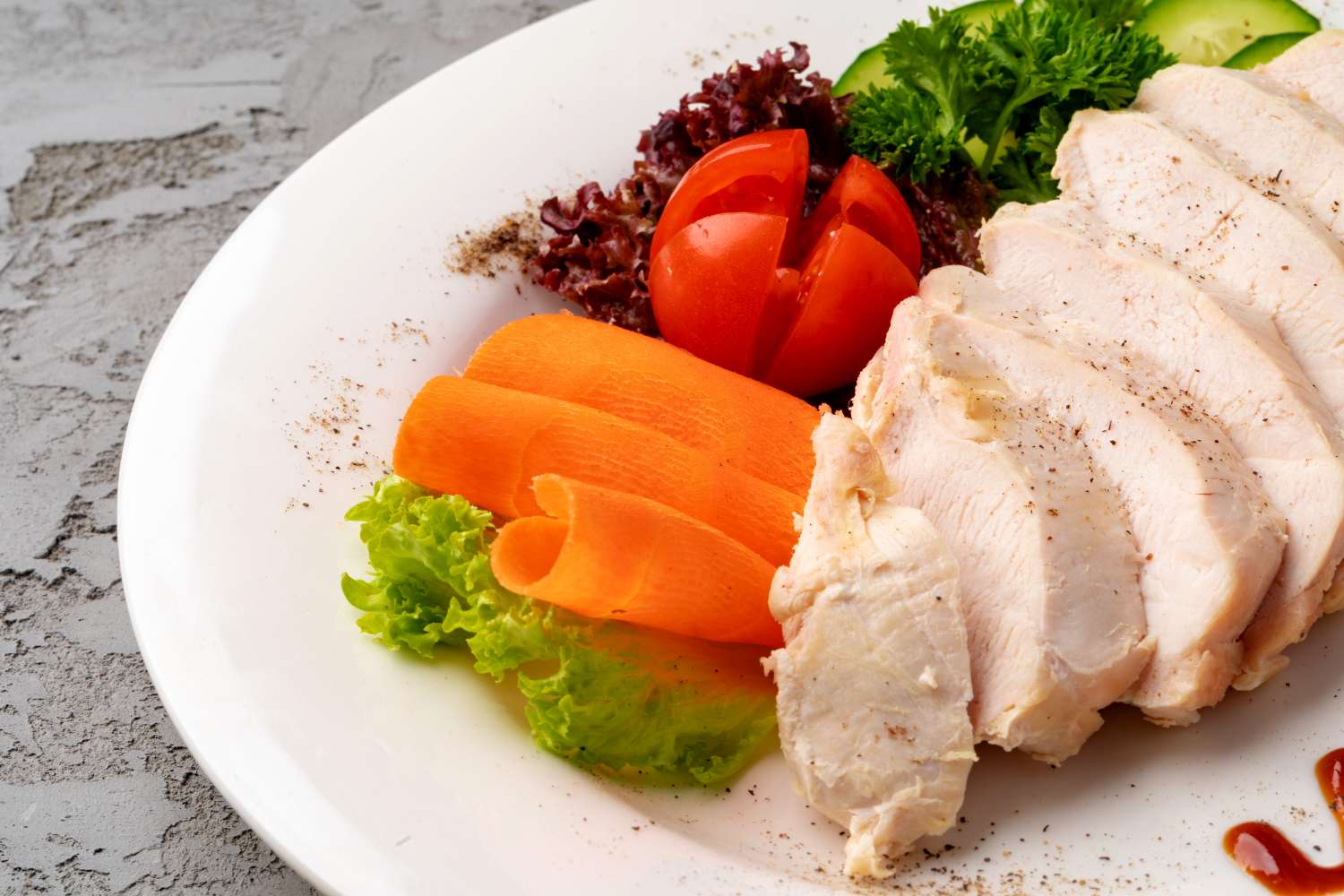 Sliced poached chicken on a plate with garnishes of lettuce carrot slices tomato and parsley