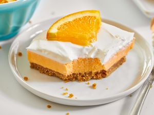 Creamsicle dessert bar with a graham cracker crust orange filling whipped topping and an orange slice garnish on a white plate