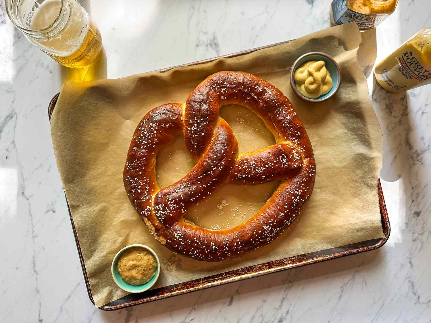 A freshly baked soft pretzel on a parchment-lined tray with mustard dips nearby