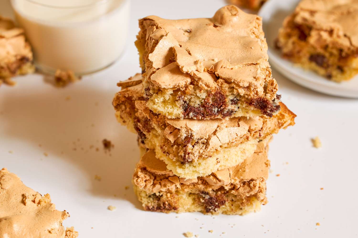 Stack of dessert bars with a meringue top and chocolate chips on a tabletop near a glass of milk