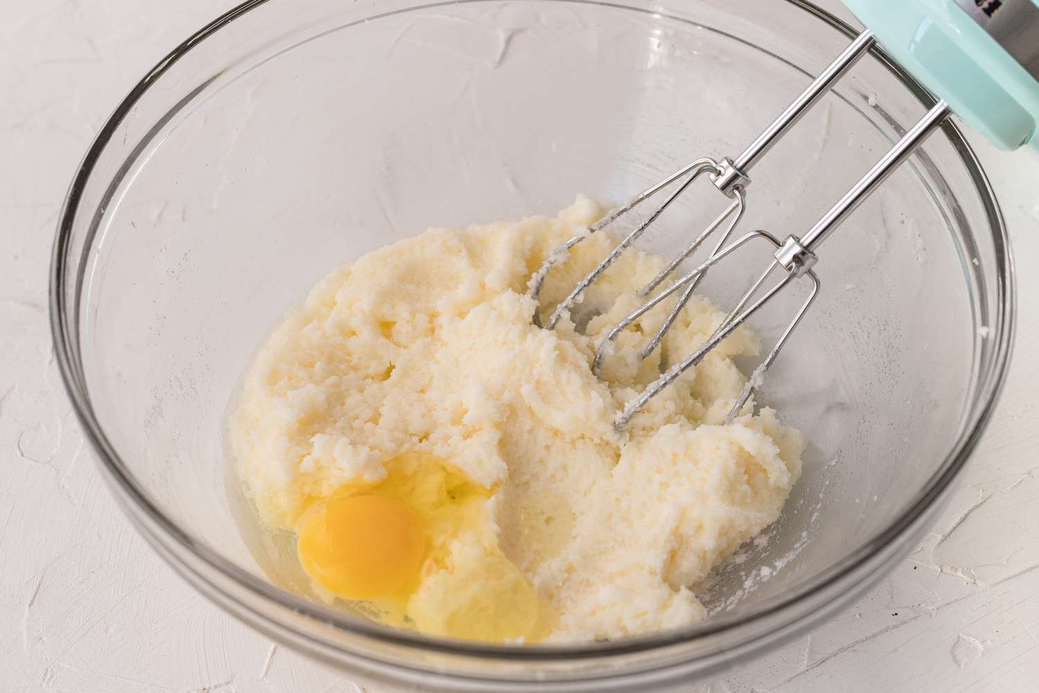 A glass bowl with hand mixer adding eggs to make a banana cookie recipe.