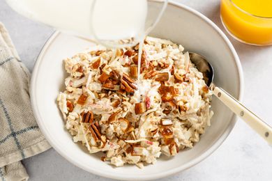 Overhead shot of a bowl of muesli with a spoon, and milk getting poured in from a glass