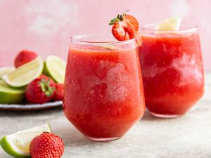 Frozen Strawberry Daiquiri in Stemless Wine Glasses Next to a Sliced Limes and Strawberries