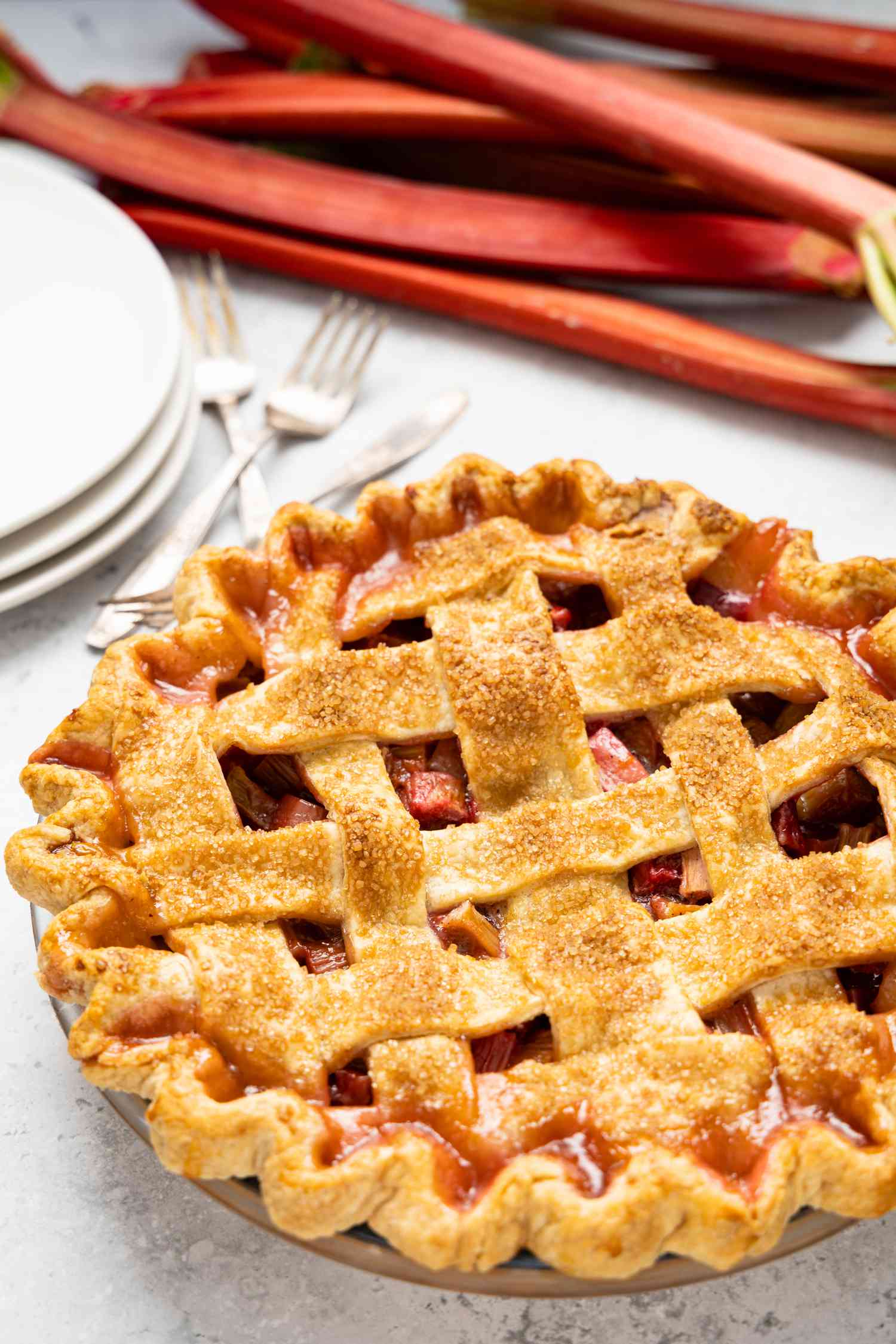 Rhubarb Pie in a Pie Dish with Plates, Utensils, and More Rhubarb in the Background
