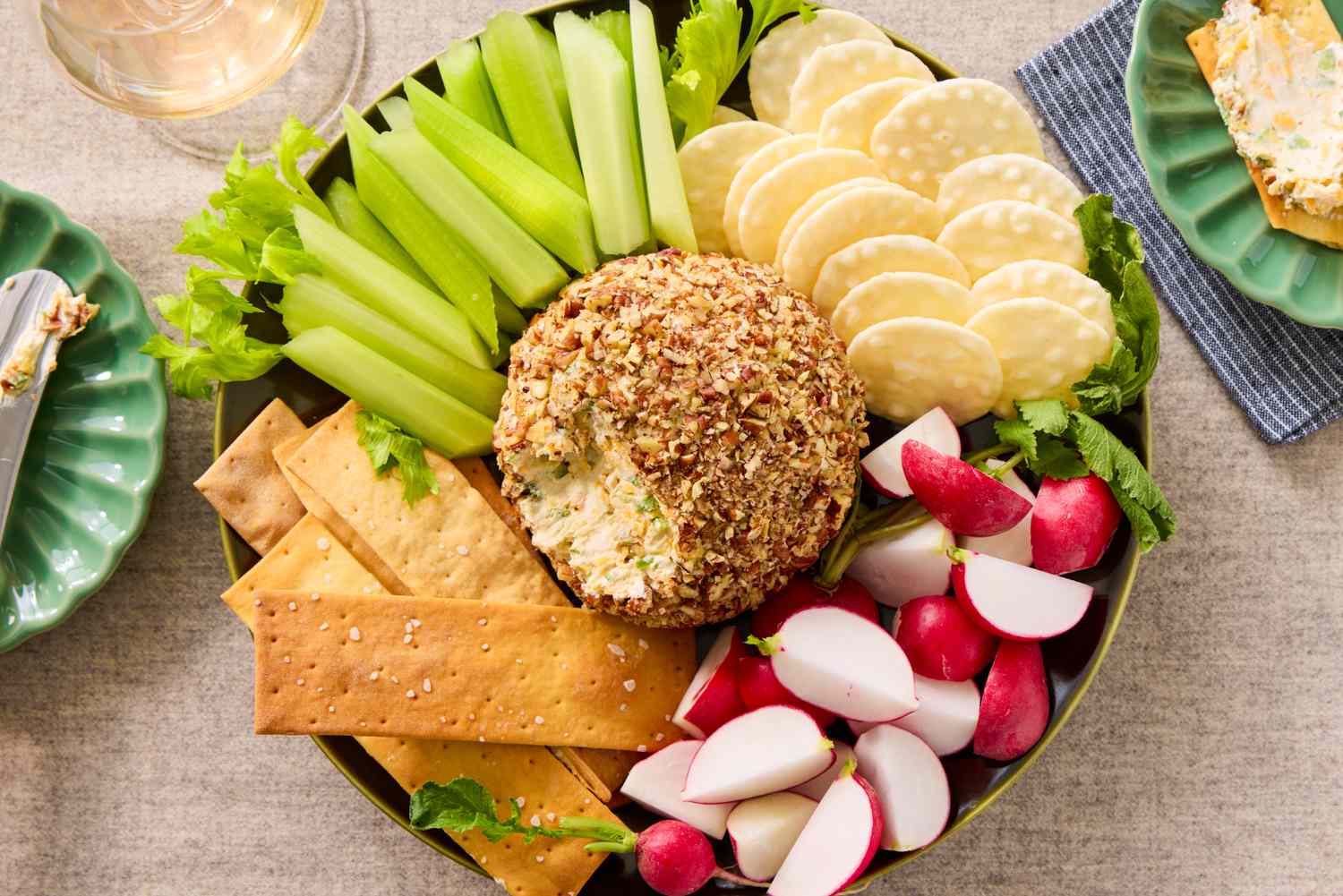 A platter with a cheese ball coated in nuts surrounded by crackers radishes and celery