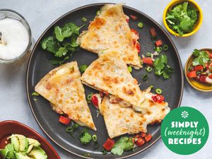 Wedges of quesadilla on a grey plate with cilantro, salsa, and avocado on the side