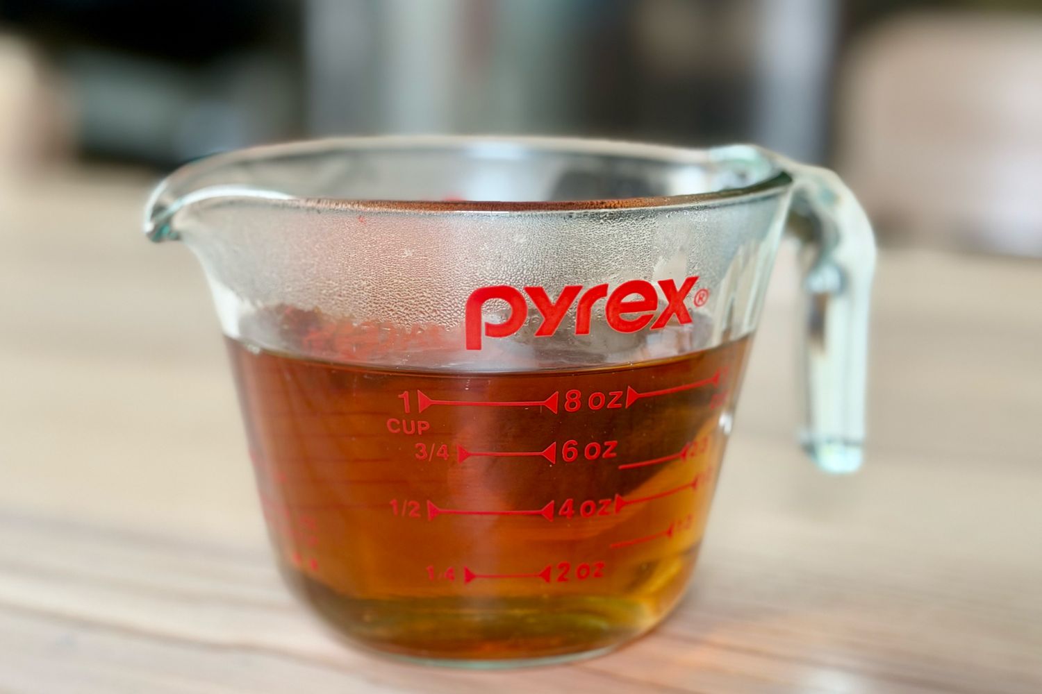 Pyrex measuring cup filled with liquid on a wooden surface