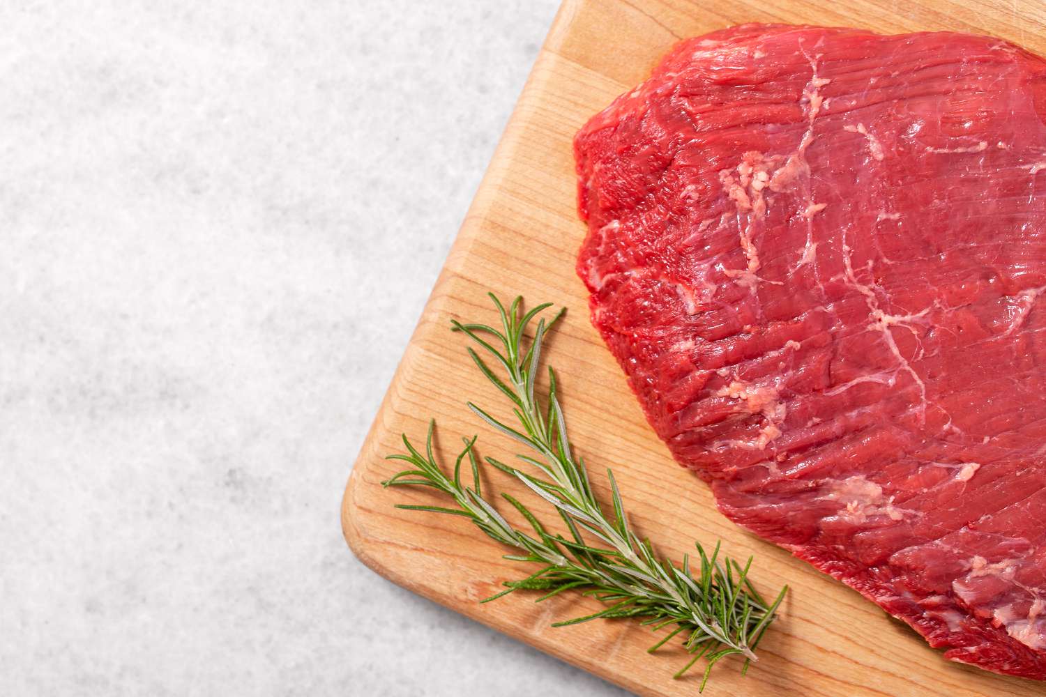 close up of a cutting board with a flank steak and two sprigs of rosemary