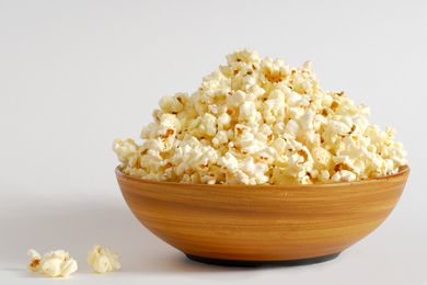 Side view of a large wooden bowl piled high with popcorn on a white background