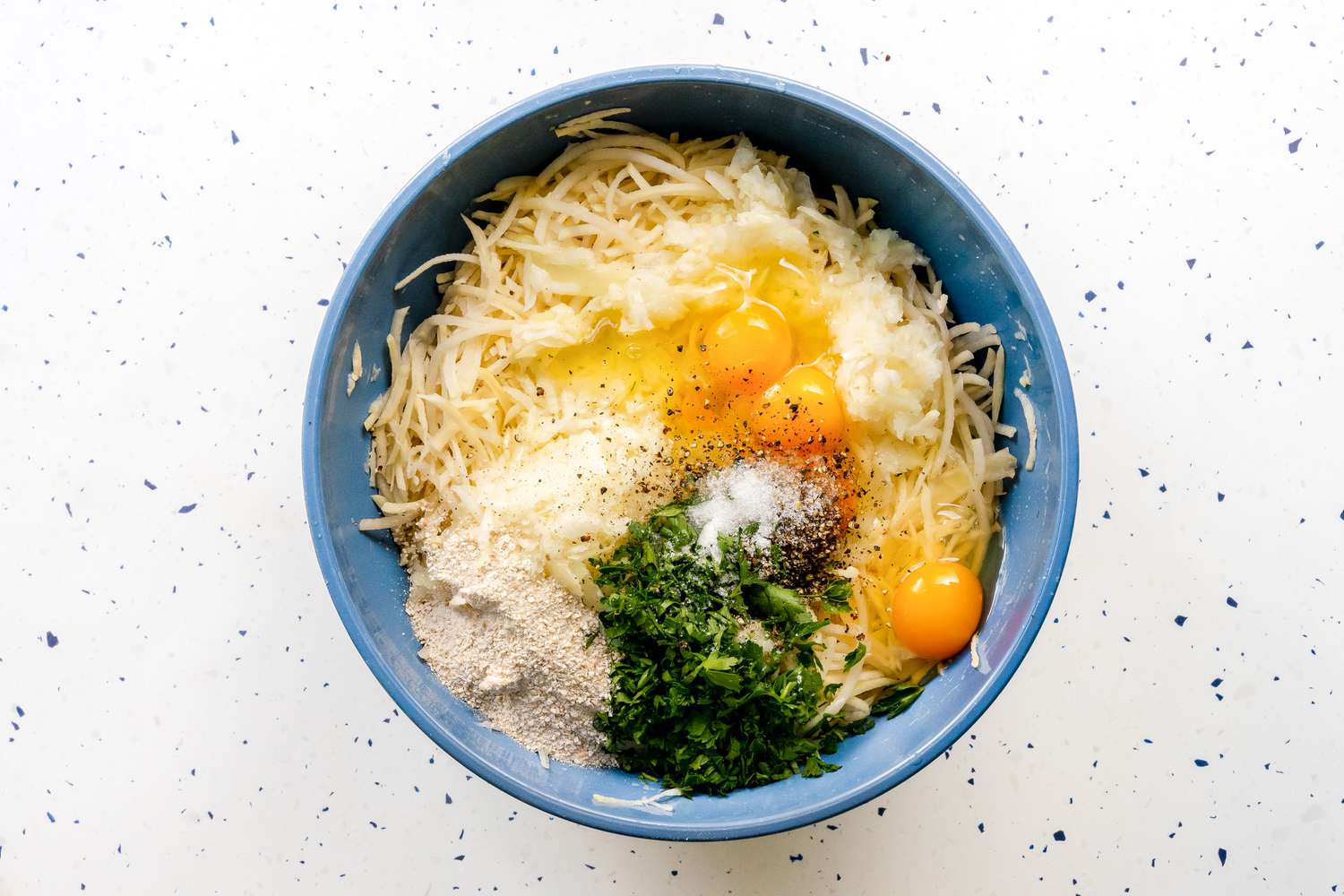 Potato Kugel Ingredients in a Bowl (Herbs, Grated Potatoes, Eggs, Matzo Meal, and Seasoning) for Passover Recipe