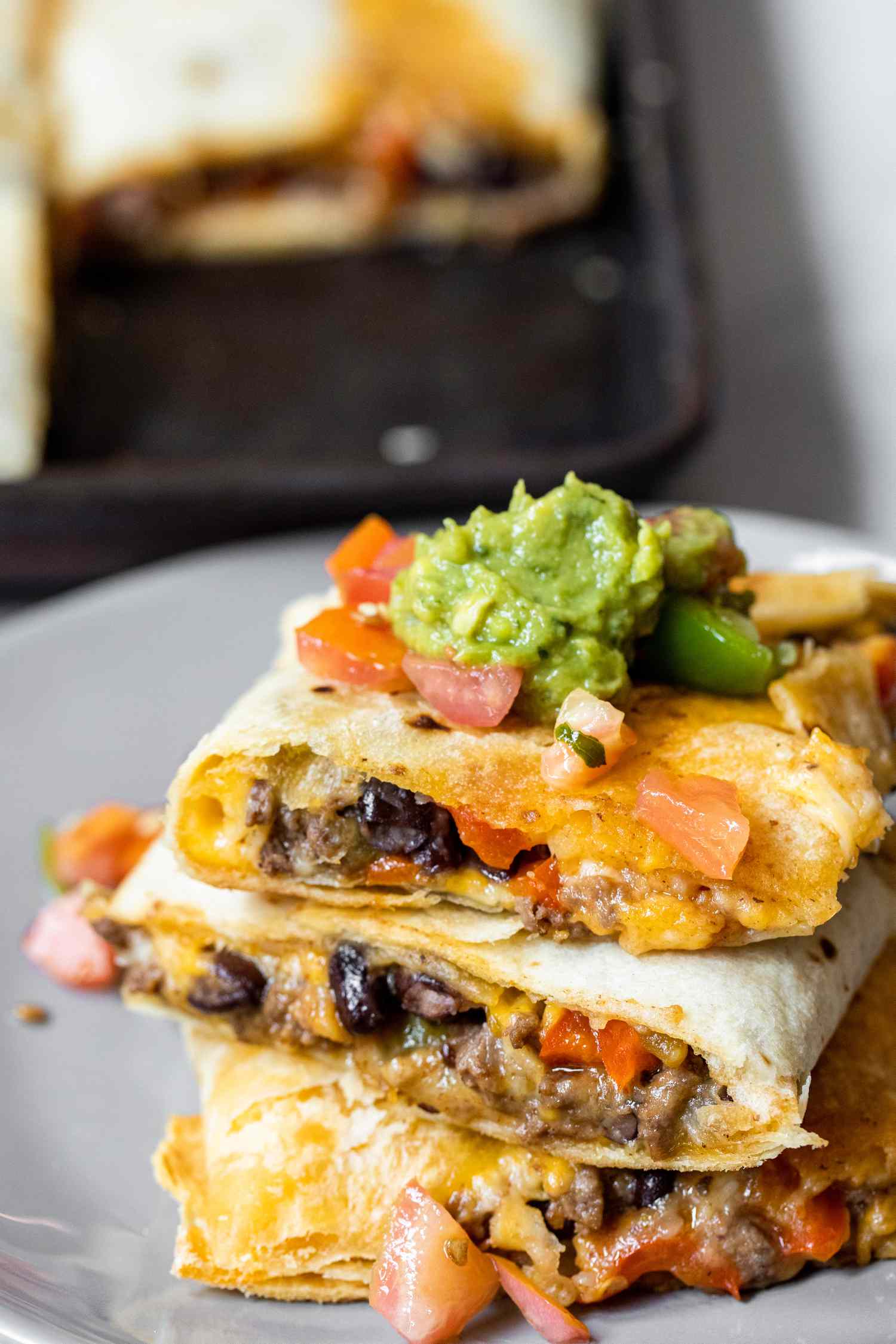 Stack of Loaded Sheet Pan Quesadillas Pieces on a Plate Topped with Salsa and Guacamole