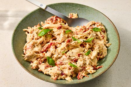 A bowl of chicken salad garnished with basil leaves, served with a spoon