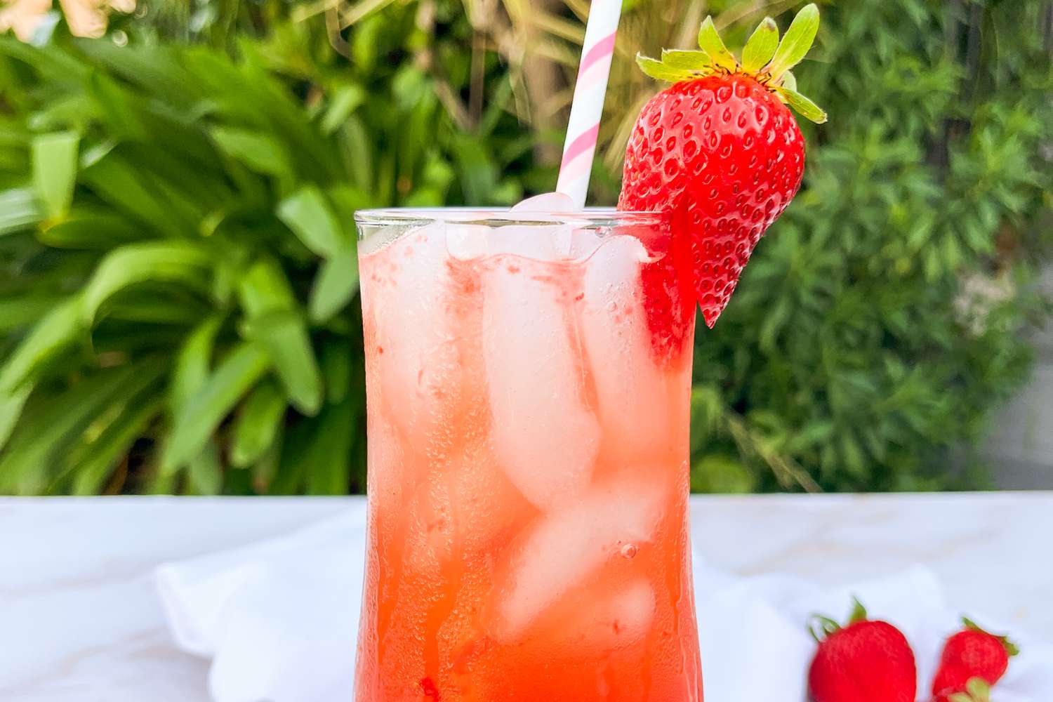 Trader Joe's strawberry smash cocktail in a tall glass garnished with a strawberry and straw