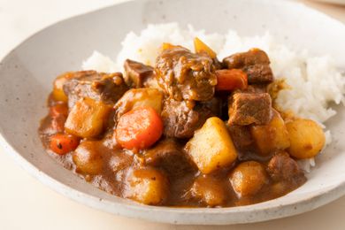 A serving of Korean curry rice with chunks of meat, potatoes, carrots, and curry sauce next to steamed rice