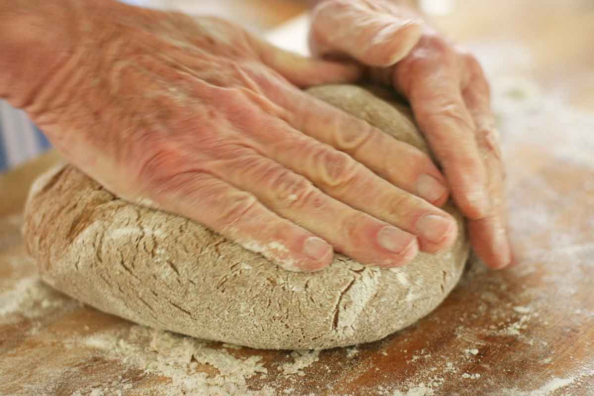 Hands shaping rye bread dough on a wooden table