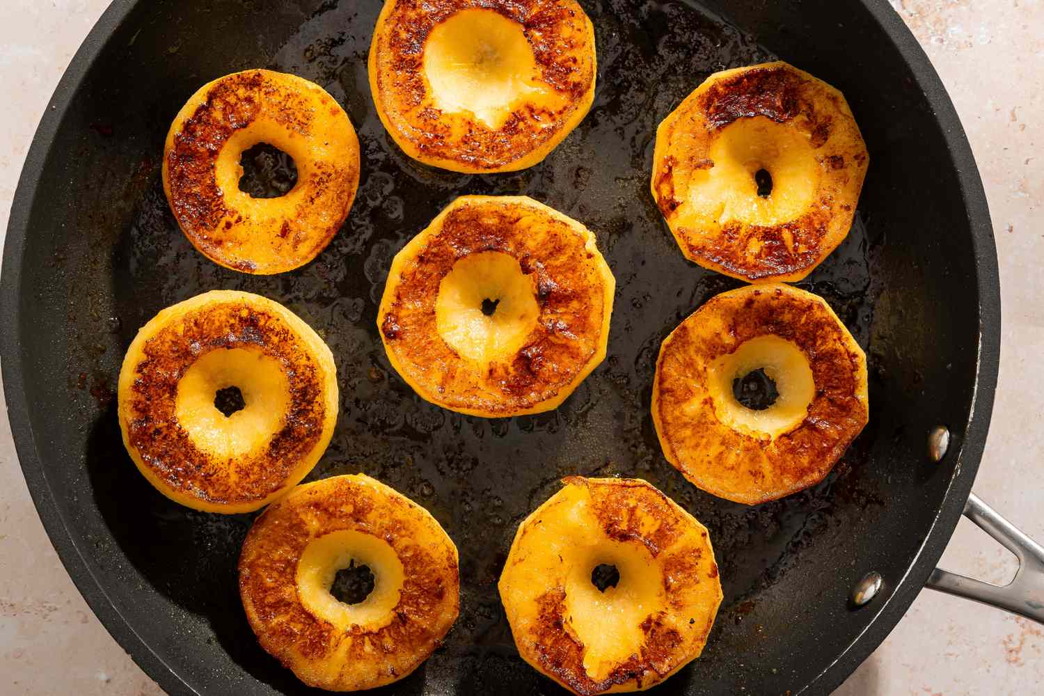 Cooked round slices of apples in a frying pan caramelized on the surfaces arranged to show both sides