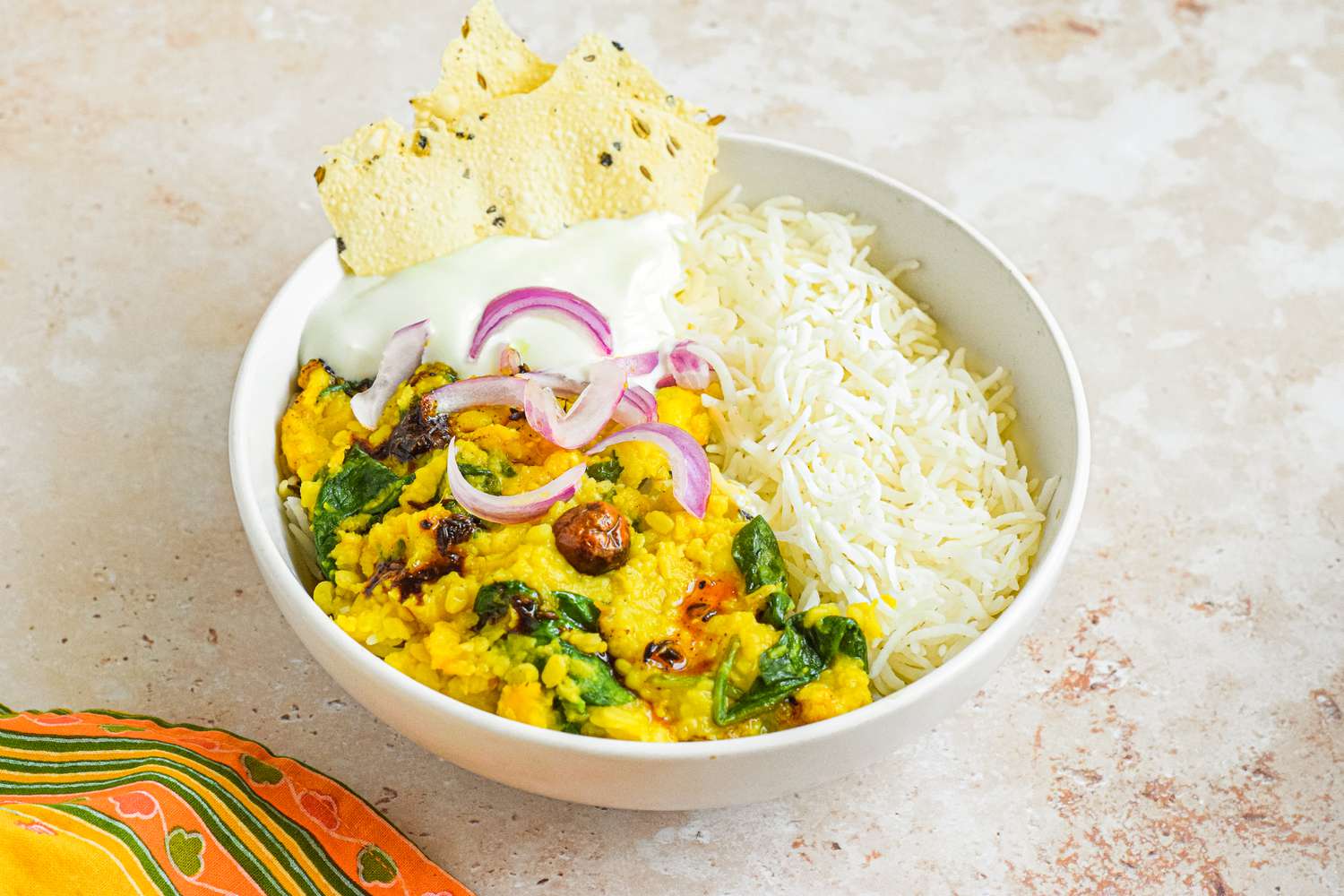 Bowl of Daal Palak over Rice Topped with Onions and Yogurt, Served with Pieces of Papad