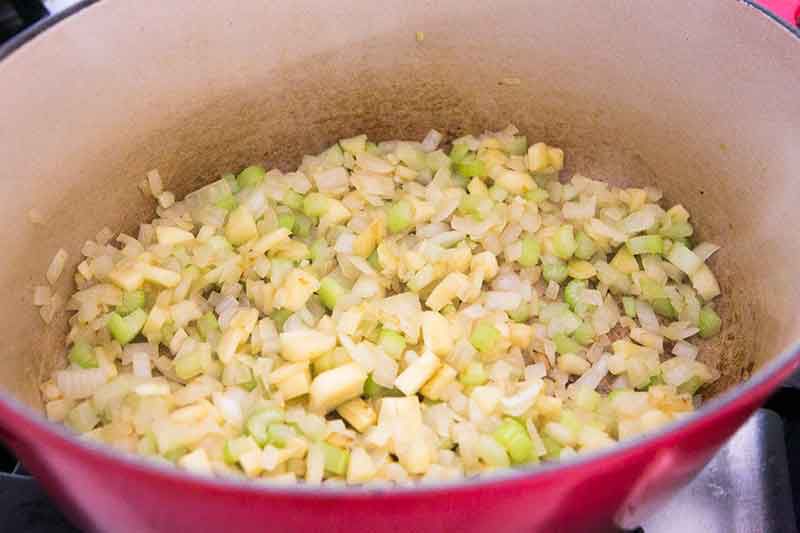 Large red cooking pot full of chopped onions, parsnips, and celery