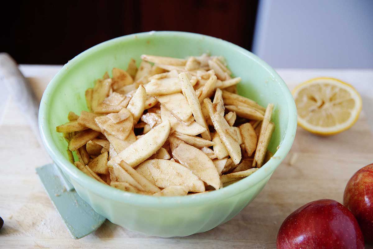 A bowl of sliced apples dressed in cinnamon, clove, lemon juice and sugar are waiting to be poured into the best dutch apple pie.