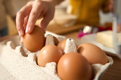 A hand reaching for an egg in a carton background has blurred kitchen elements