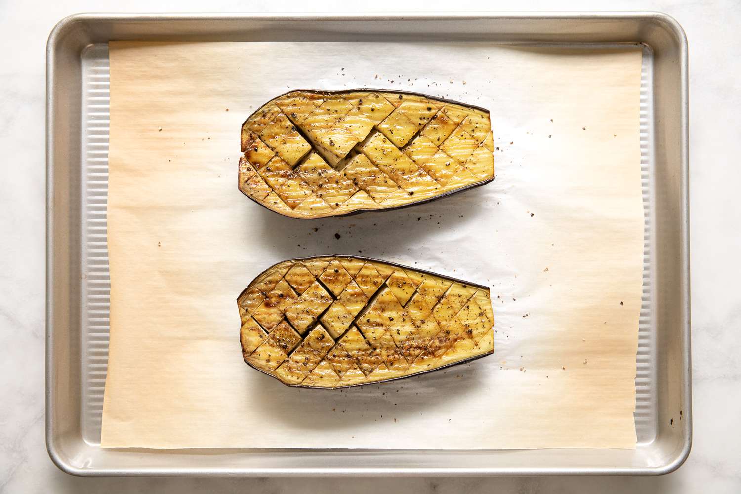 Eggplant Halves Flipped With Score Side Facing up on a Parchment Lined Baking Tray