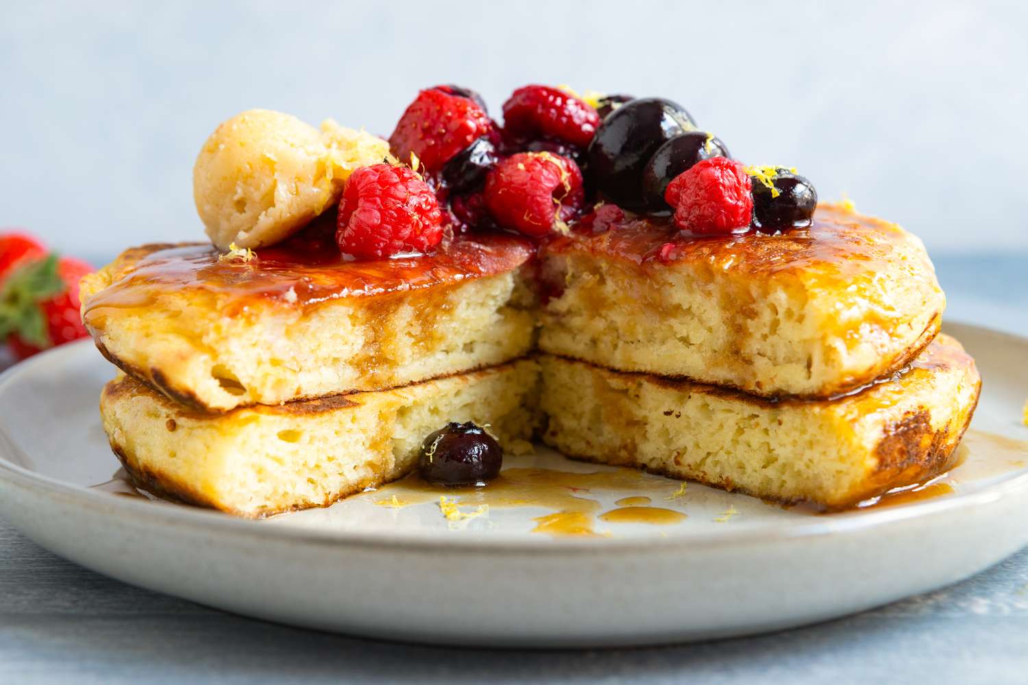 Stack of pancakes topped with berries and a scoop of butter