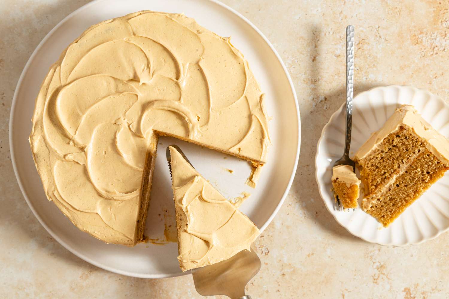 A frosted cake with one slice cut out served on a plate beside it with a fork