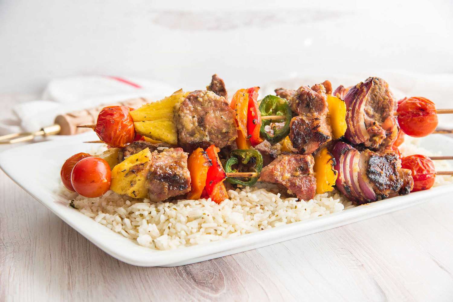 Pork kebabs with grilled pineapple and a rainbow of vegetables are on a platter along with rice.