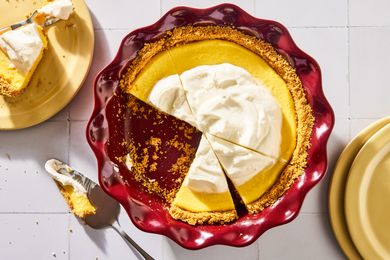 A pie served in a red dish with whipped topping and a slice removed on a table with plates nearby