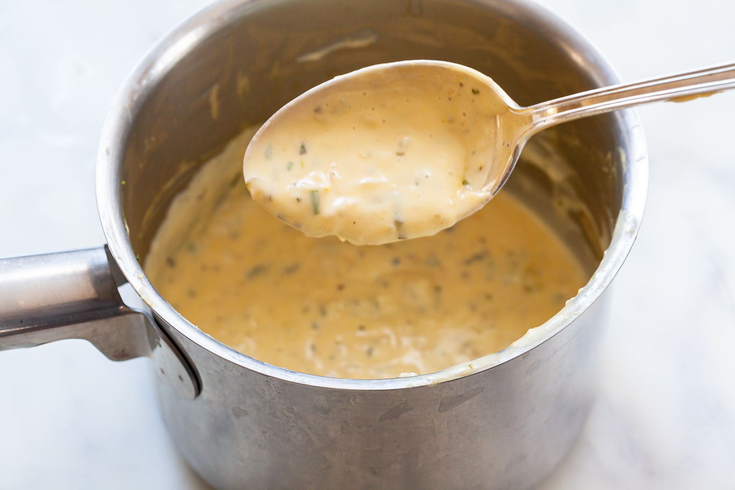 Classic mother sauce: béarnaise in a pan with a spoon coated in sauce above the pan.