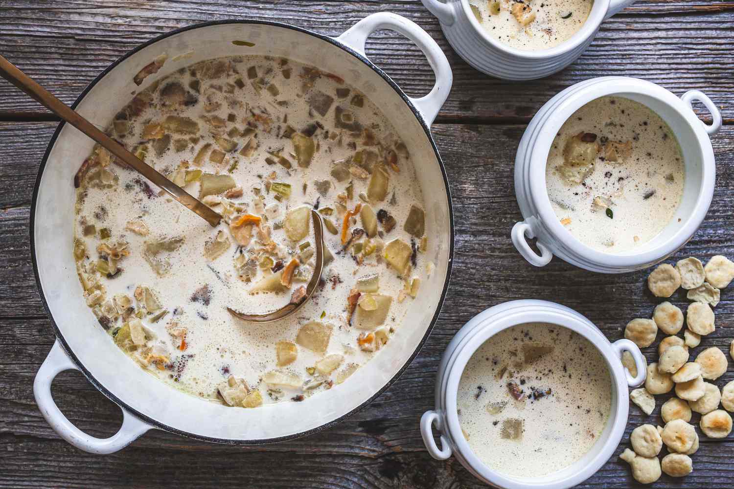 Classic New England Chowder in a Dutch Oven and in Individual Soup Bowls with Handles, Next to Oyster Crackers on the Table
